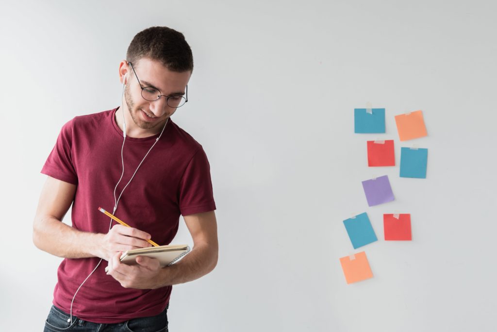 Jovem anotando ideias em seu caderno e post-it para realizar seu planejamento pessoal